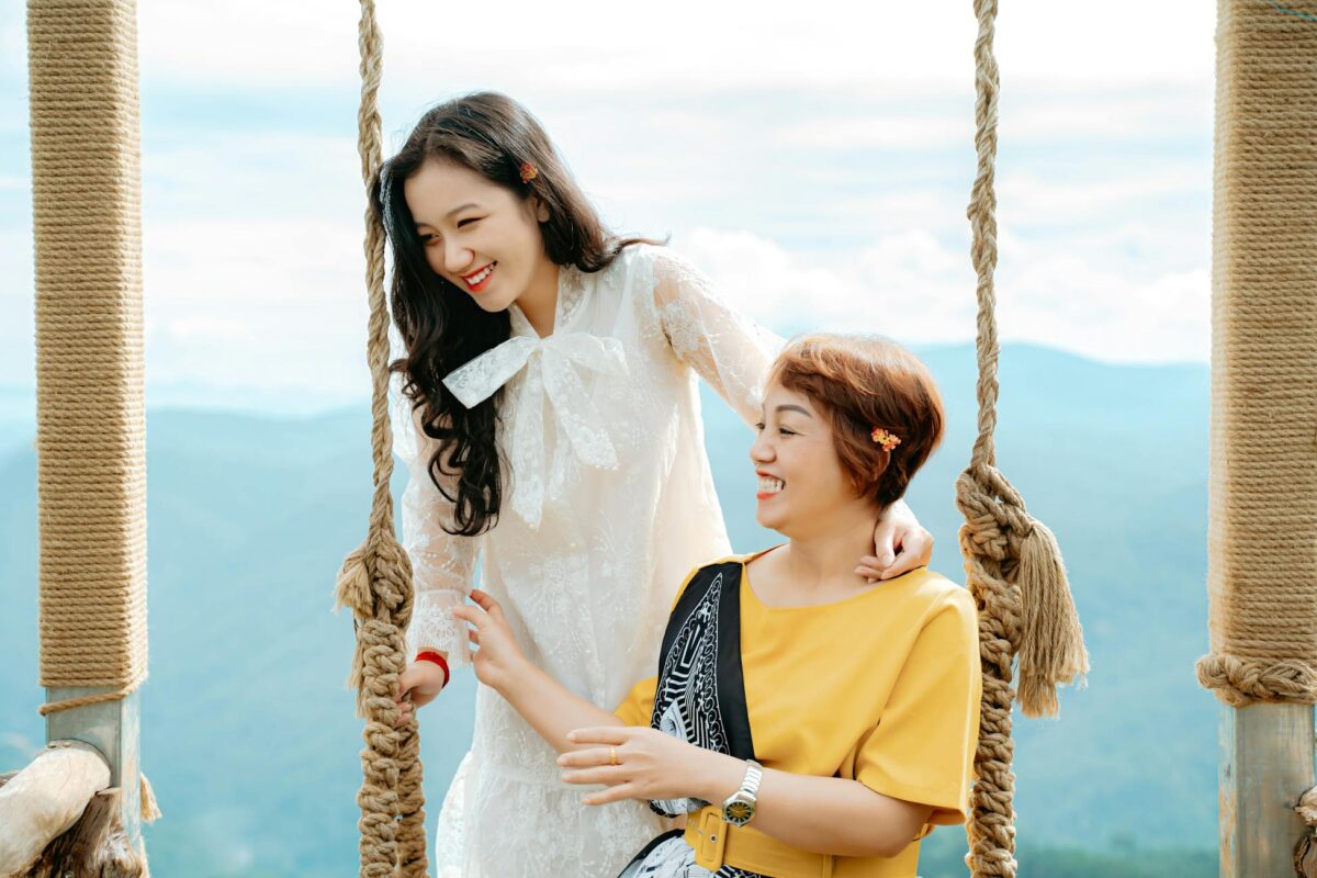 A happy mother and daughter enjoying a day out on a swing with mountain views.