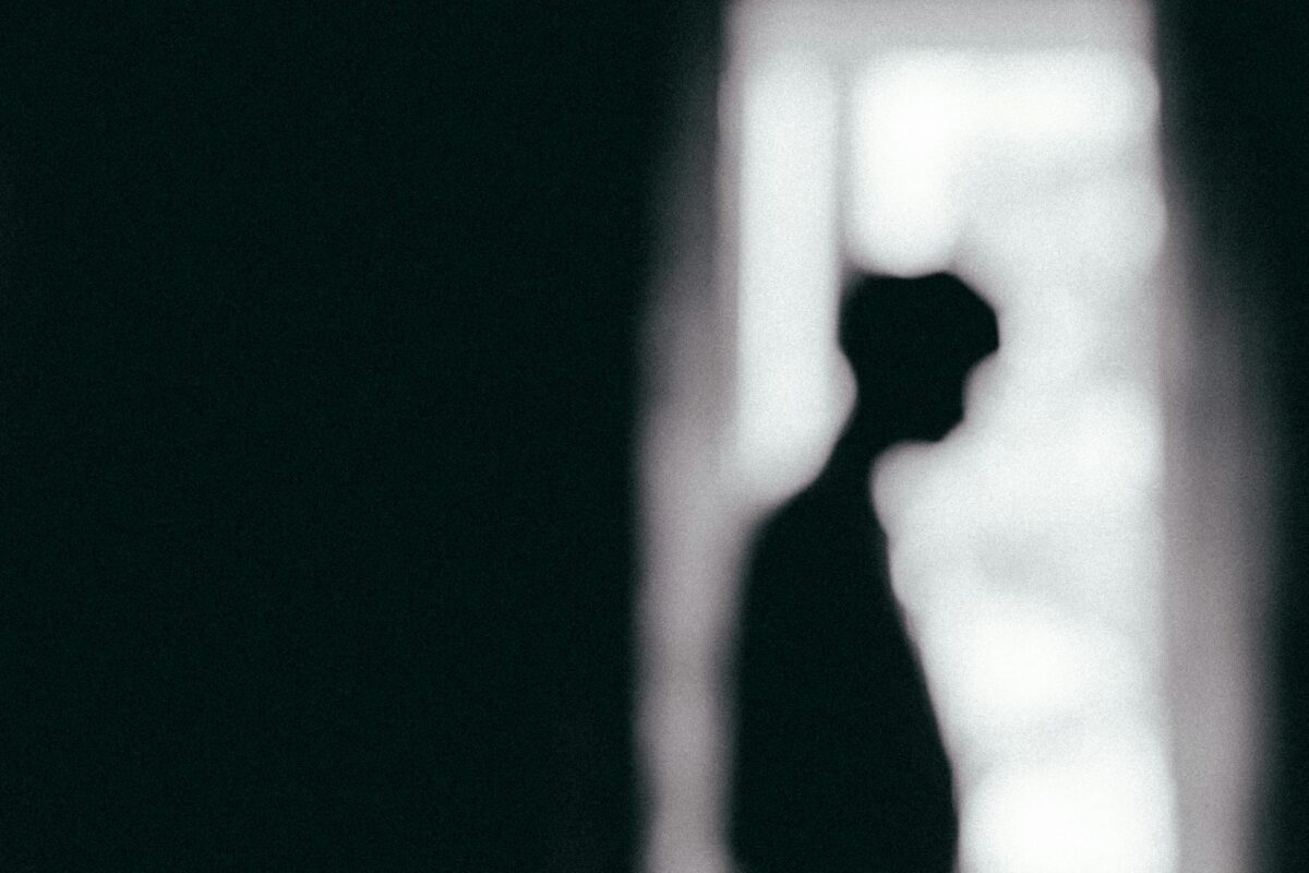 Moody black and white silhouette of a person standing by a window, conveying solitude.