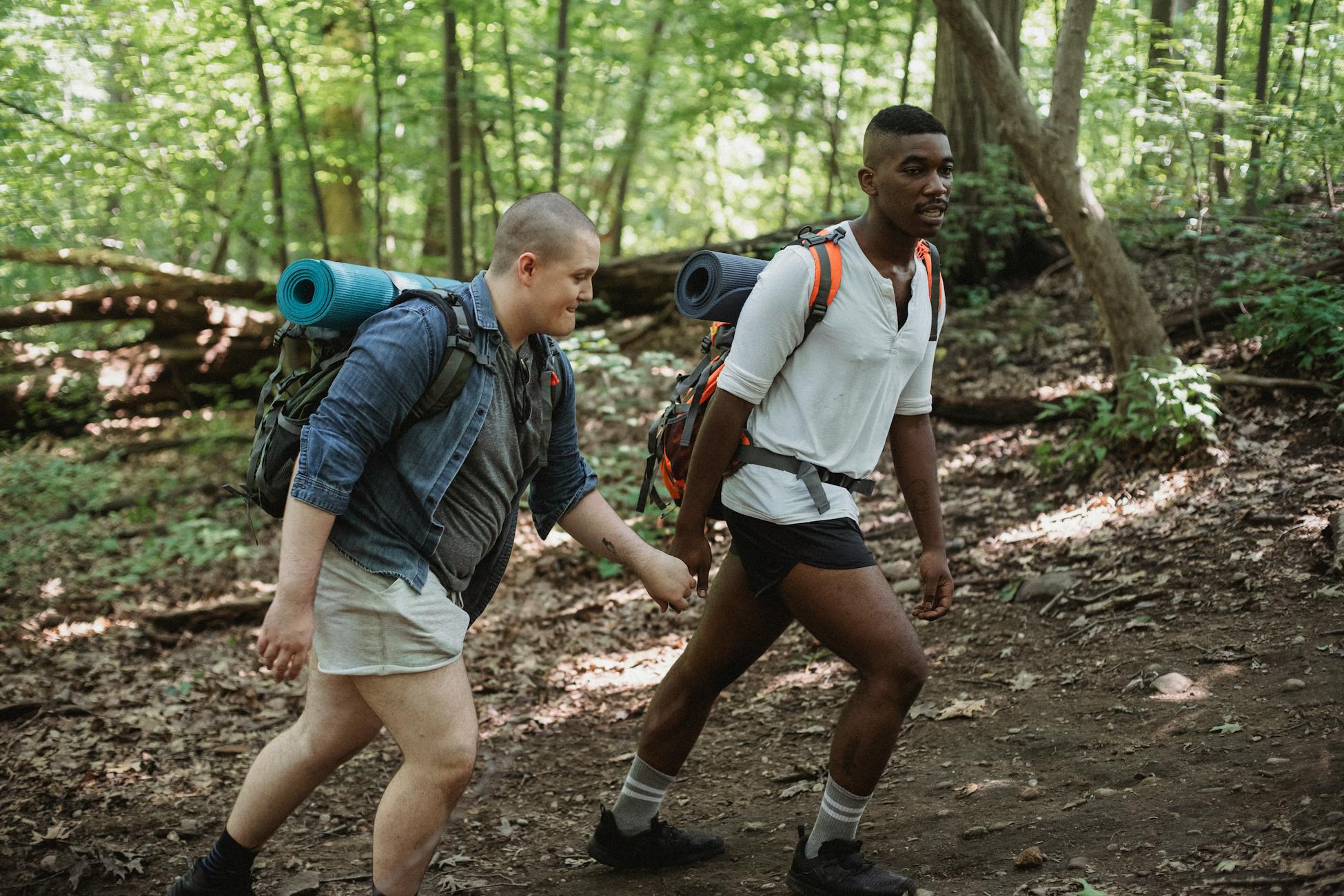 Same sex diverse couple with trekking equipment holding hands while traveling in forest