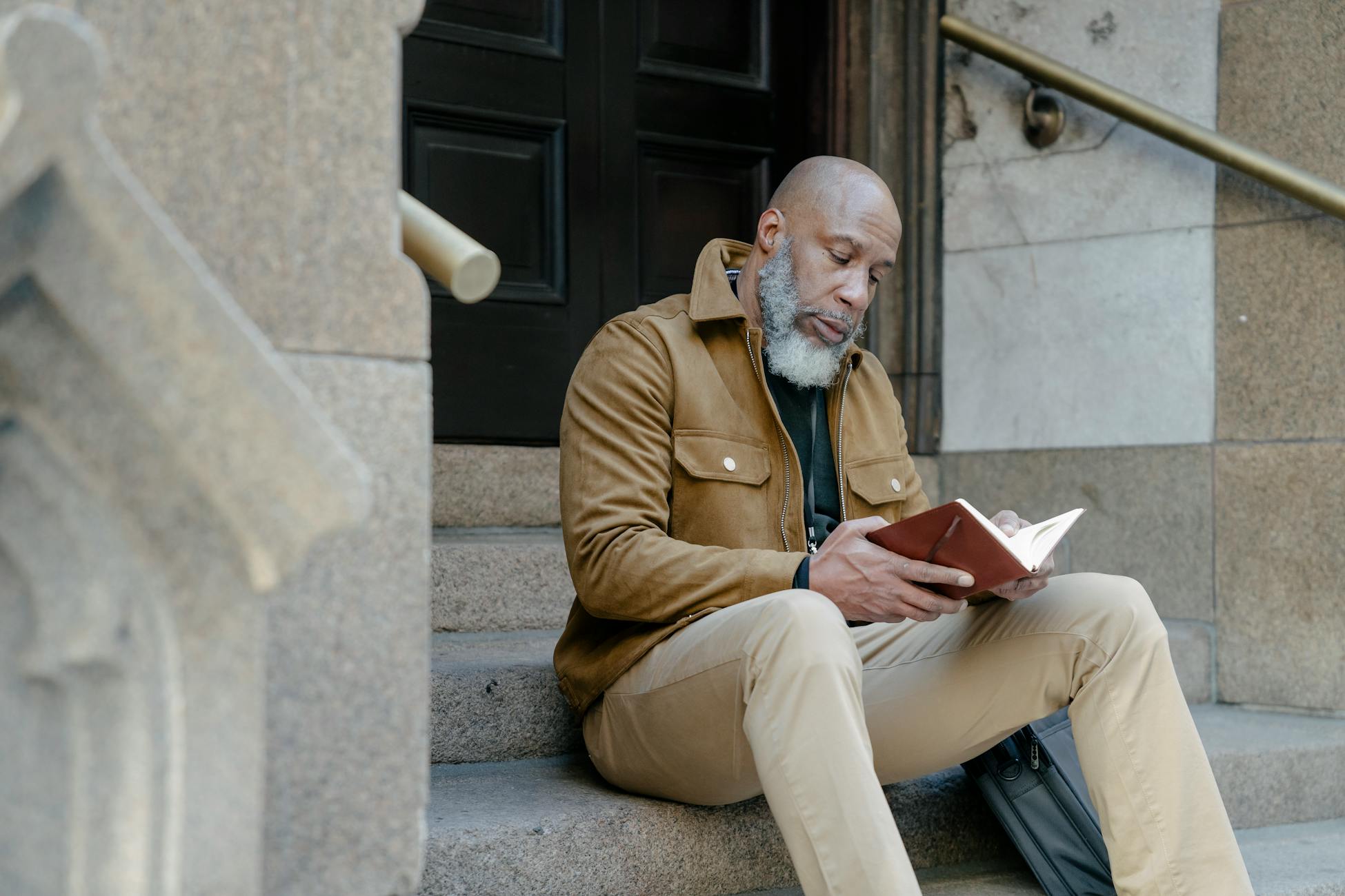 A mature African American man sitting on stone steps engrossed in reading a book.