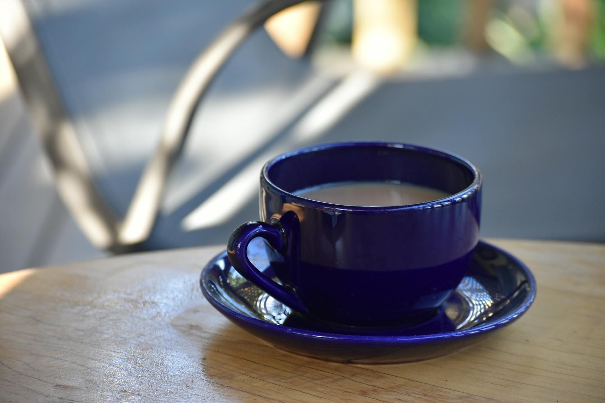 A vibrant blue coffee cup sits on a wooden table, capturing a moment of relaxation outdoors.