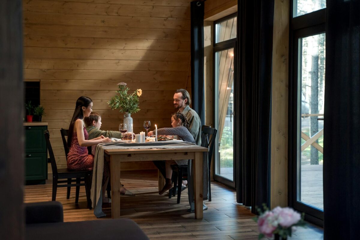A family enjoying dinner in a cozy, modern wooden cabin with warm lighting.