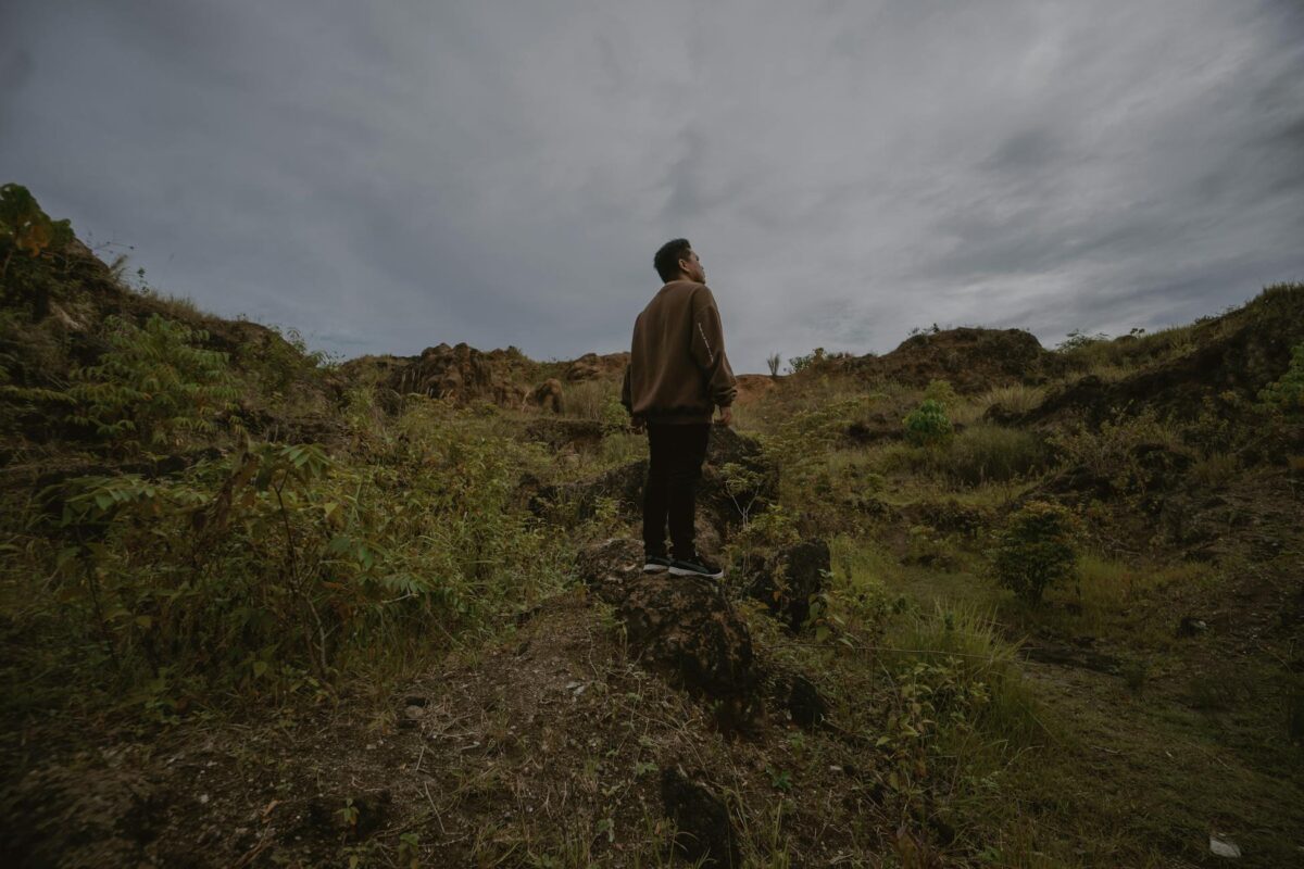 A man standing outdoors on rocky terrain, contemplating nature under a cloudy sky