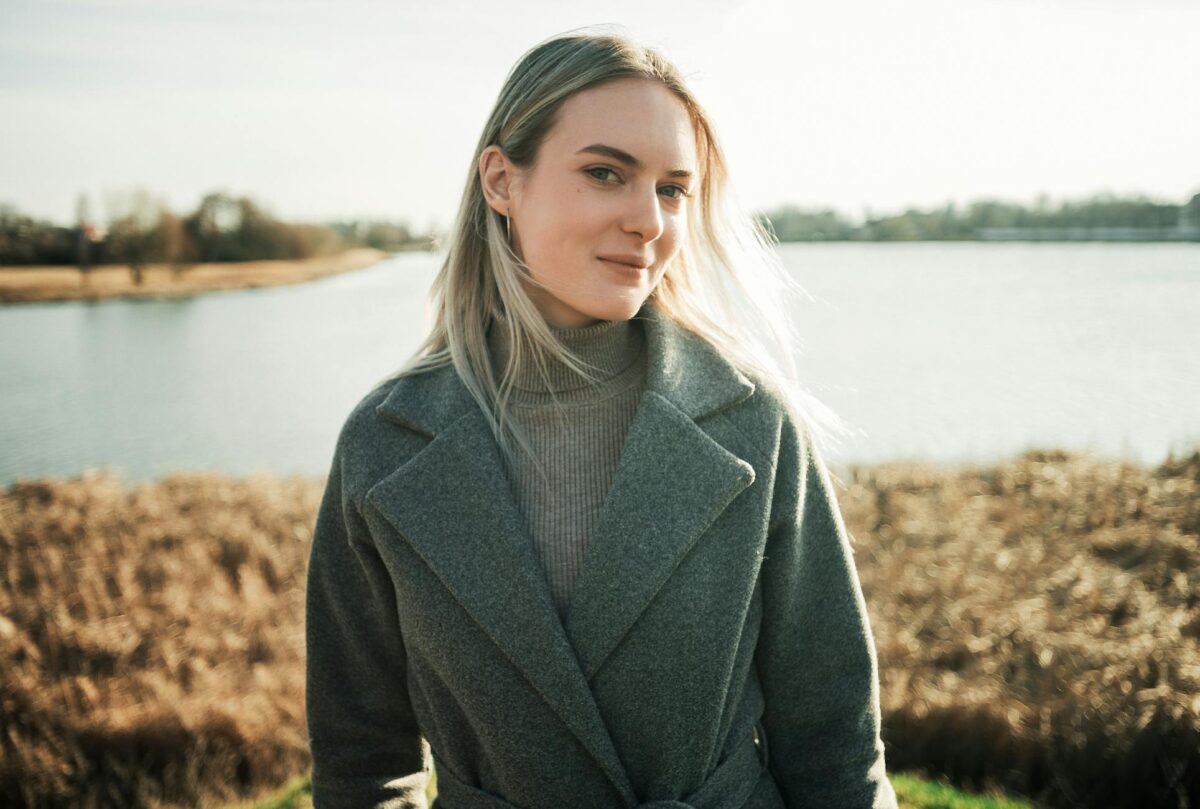 Portrait of a woman in a grey coat by a serene lake, capturing a calm autumn day.