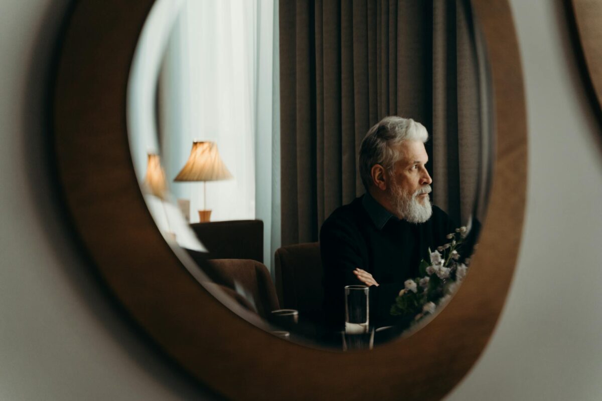 An elderly man gazes thoughtfully in a cozy, modern room with a warm ambiance.