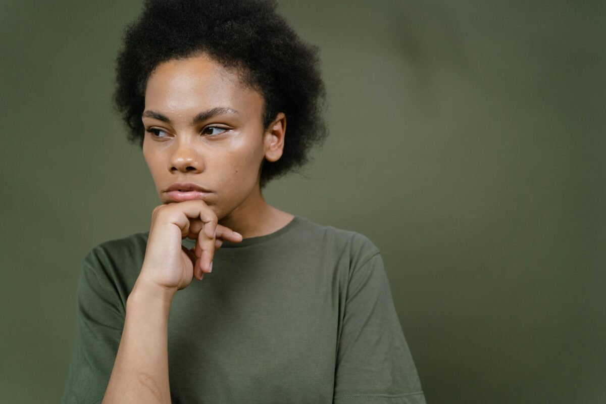 A pensive young woman with afro hair contemplating and looking away, emphasizing individuality and emotion.