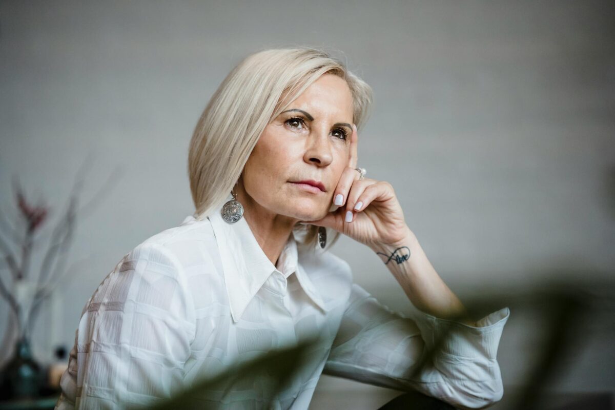 Portrait of a well-dressed senior woman lost in pensive thought indoors.