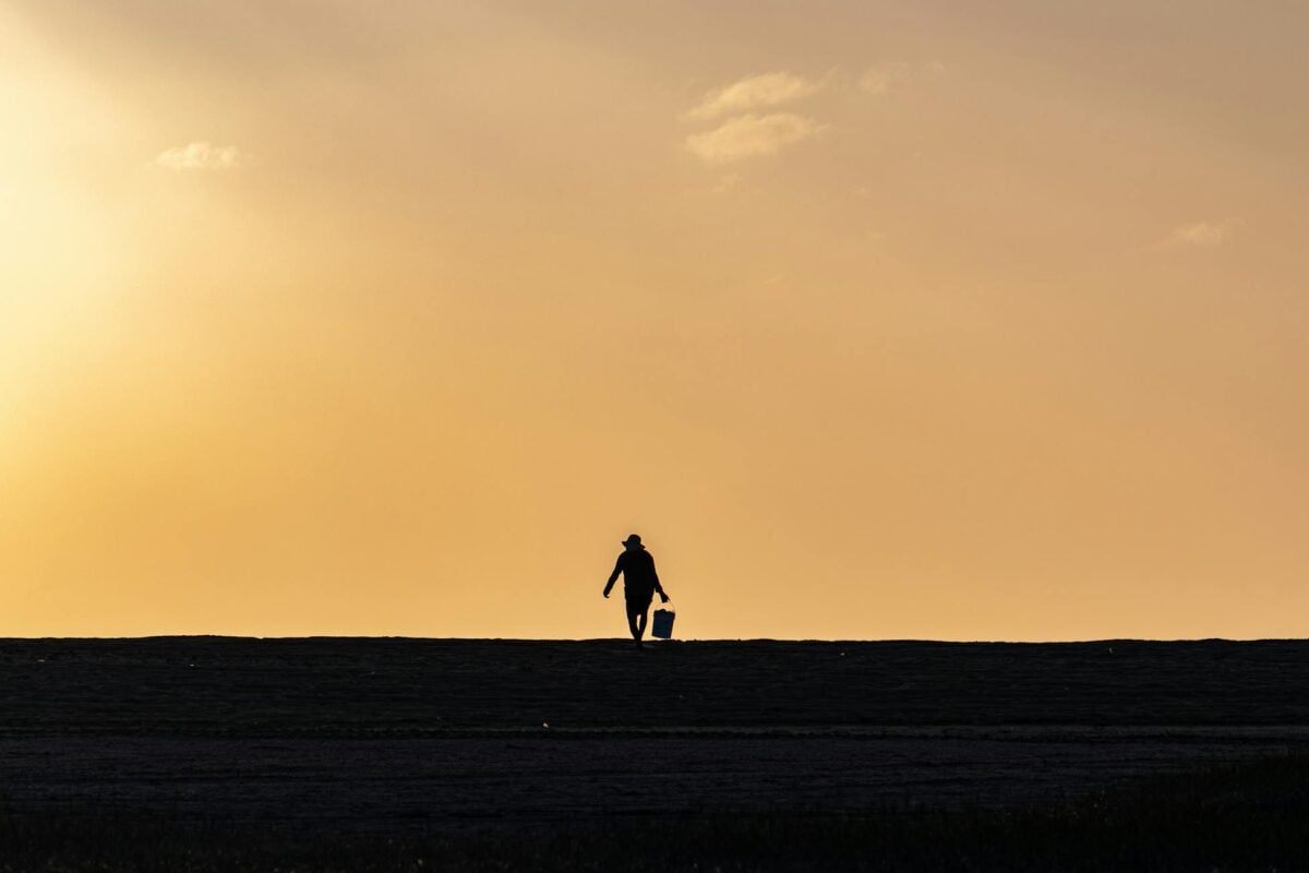 A person silhouetted against a sunset sky in RJ, Brazil, carrying a bucket.