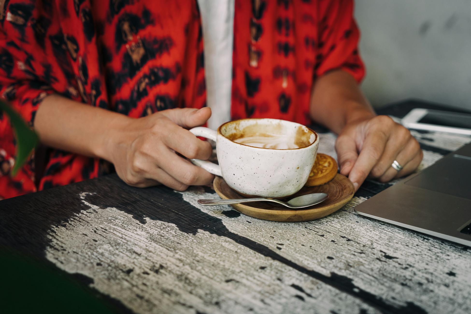 A person holding a coffee cup at a rustic café table, ready for work or relaxation.