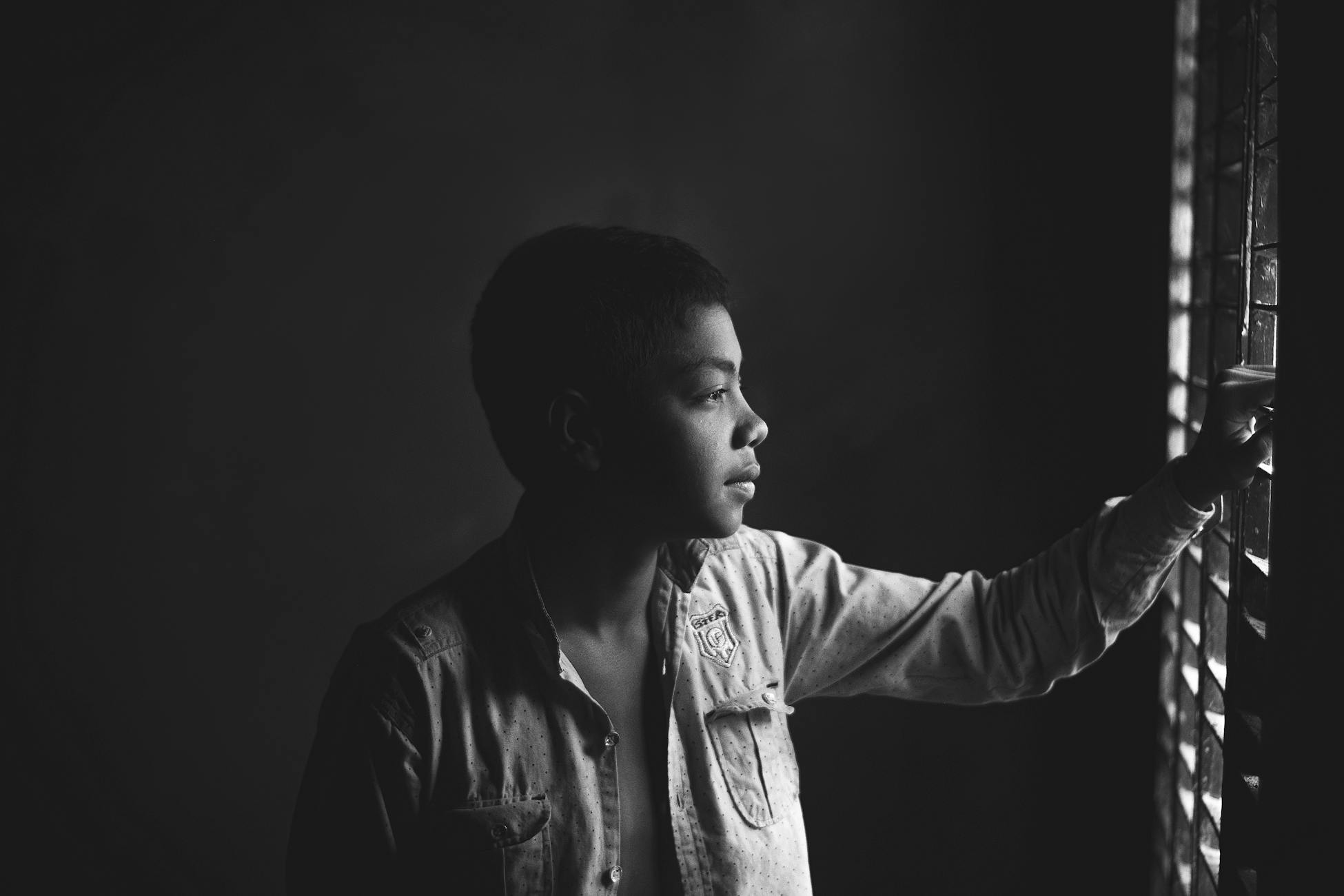 Thoughtful black and white portrait of a boy looking out the window.