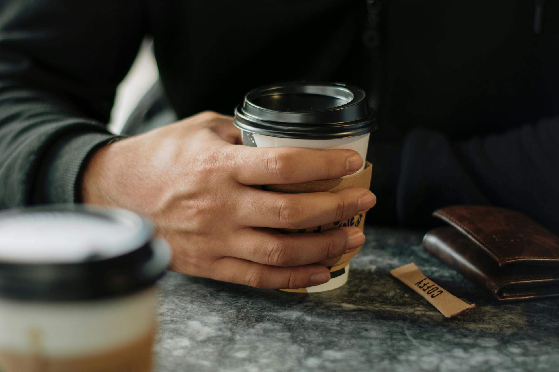 A close-up of a man's hand holding a to-go coffee cup inside a cafe.