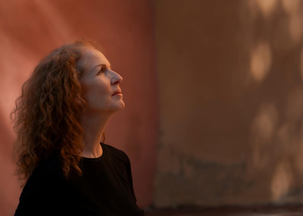 Profile portrait of an elegant mature woman with curly red hair against a warm background.