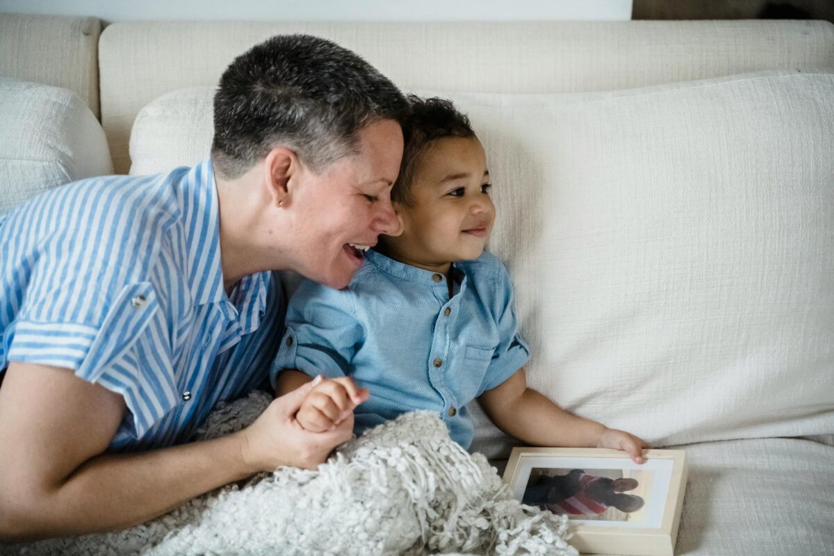 A warm, candid moment of a mother smiling with her child on the sofa holding a family photo.