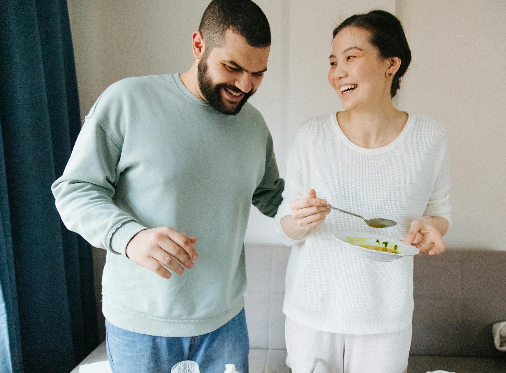 A smiling couple sharing a joyful moment during a meal in a cozy indoor setting.