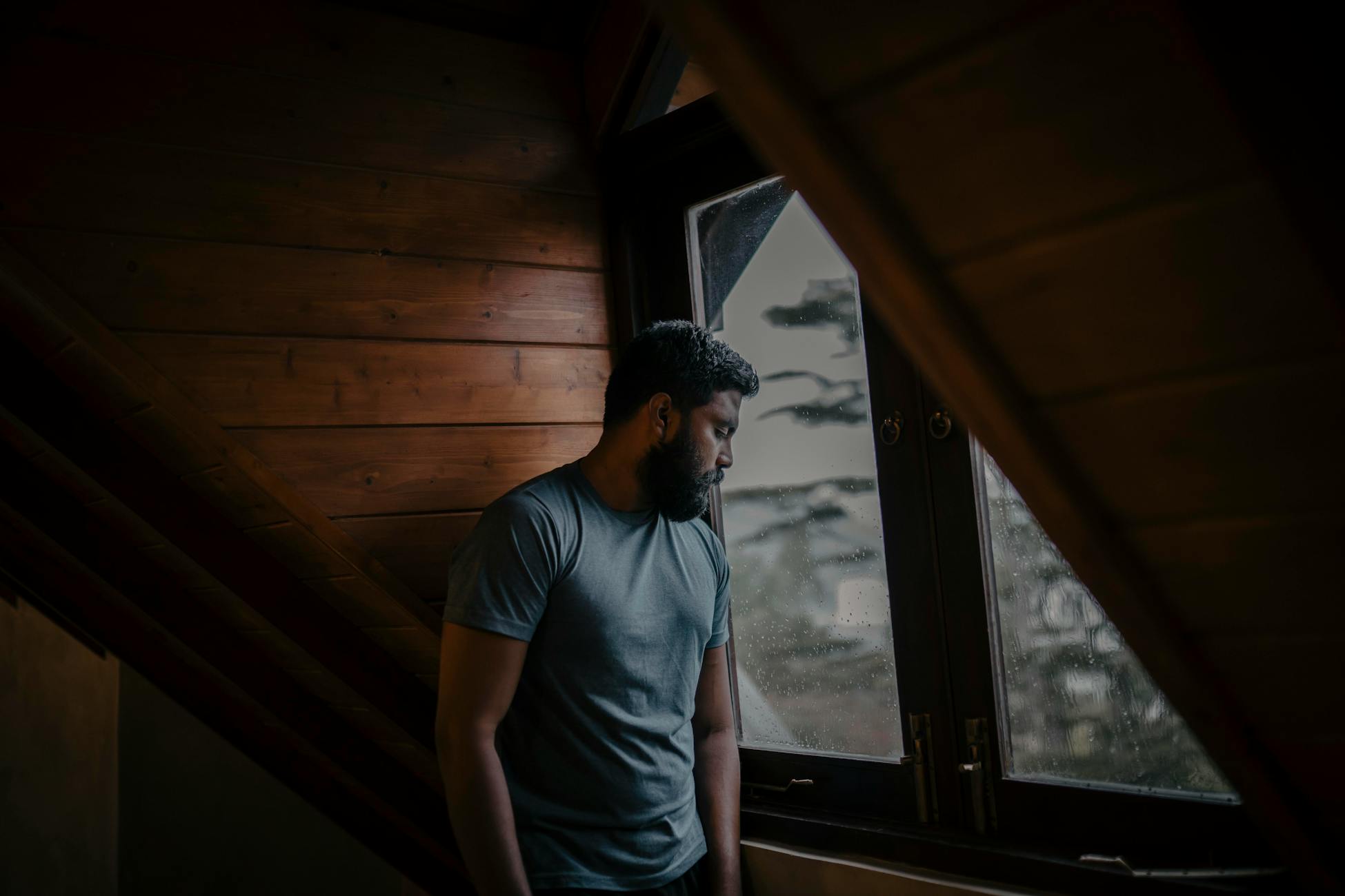 A thoughtful man stands by a window, lost in contemplation, indoors in Sri Lanka.